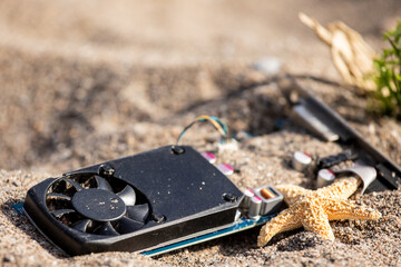 A obsolete computer video card buried in beach sand surrounded by starfish suggesting washed up old...