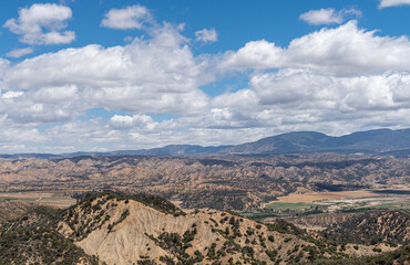 Fototapeta na wymiar Los Padres National Forest, CA, USA - May 21, 2021: Dry mountain range in eastern part under heavy blue cloudscape with agriculture in valley. Shrub vegetation.
