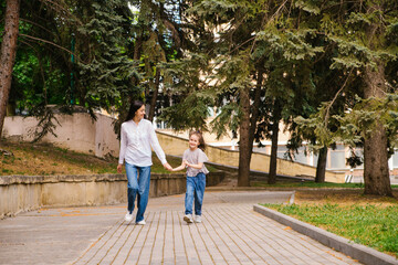 A little girl with her mother runs along the sidewalk in the park. Active play in nature.