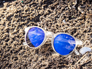 Lost blue reflective child's sunglasses lying in the sand on a beach on a sunny day