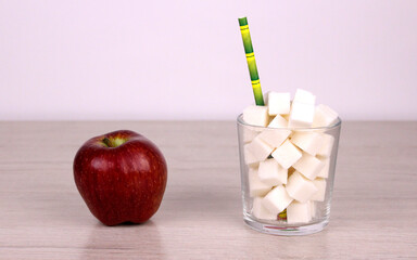 Sugar cubes in a glass with a straw and a red apple. Healthy food versus unhealthy sugary high-calorie drinks