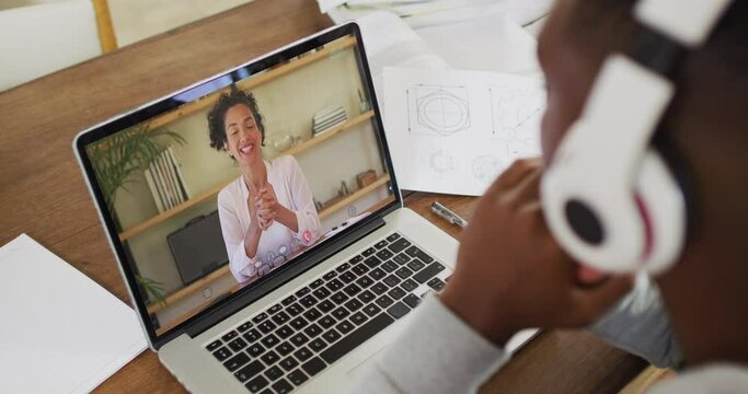 African american male college student holding notes while having a video call on laptop at home