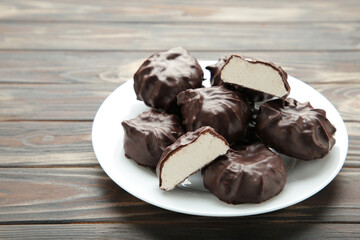 Chocolate covered marshmallows on plate on brown background.