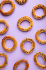 Whole bagel with poppy seeds on purple background. Vertical photo