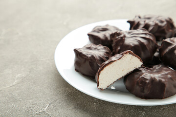 Chocolate covered marshmallows on plate on grey background.