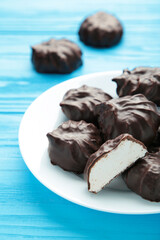Chocolate covered marshmallows on plate on blue background. Vertical photo