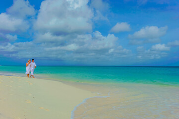 Young couple walking on the beach, in white outfits