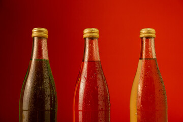 Red yellow and green glass bottles covered with small droplets stand on a red background. Refreshing drink