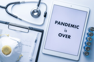 End of pandemic. Syringe with needle, hospital healthcare charts, doctor stethoscope and white tablet with text on screen for medical equipment background. Pandemic is over concept.