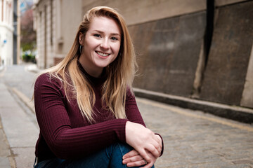 Portrait of smiling young woman looking to camera in a narrow street.