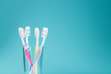 Toothbrushes of different colors in a transparent glass on a blue background.