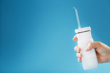 White irrigator in hand for cleaning teeth on a blue background.