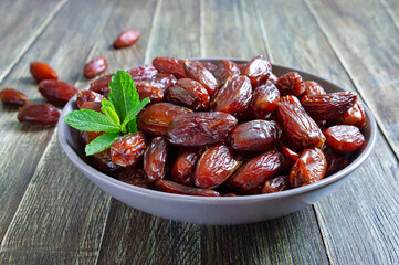Sun-dried dates in a ceramic bowl and fruits scattered on a wooden table. Organic dried fruits.