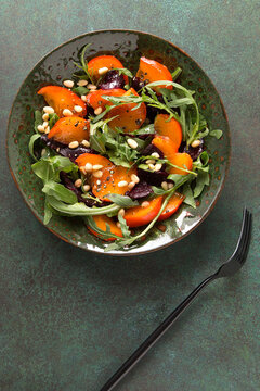 flat lay bowl with baked beetroot, arugula and persimmon salad on dark table