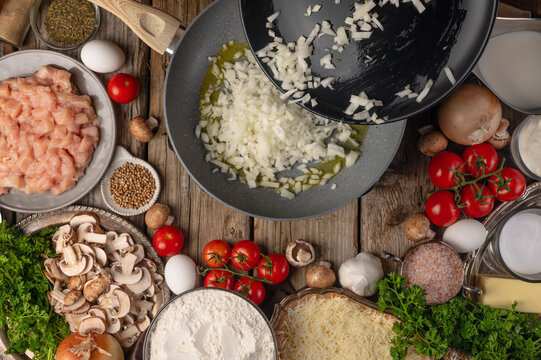 In the photo, the process of making risotto. The cook mixes the rice with melted butter. Many ingredients are laid out on a wooden table. Very bright colors. Color image. High angle view.