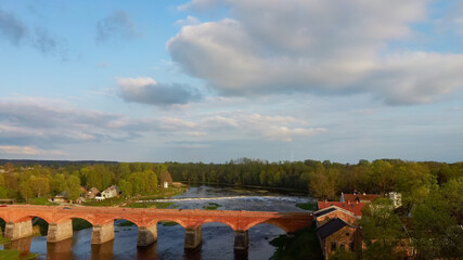 Fototapeta na wymiar Long Old Brick Bridge, Kuldiga, Latvia Across the Venta River. Captured From Above. The Widest Waterfall in Europe in Background