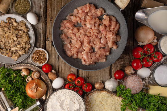 Minced meat prepared for frying in a frying pan. Foods beautifully laid out on a wooden table create a colorful still life. Healthy foods, vitamins. Color image. No people. View from above.