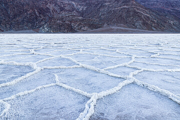 Fototapeta na wymiar Badwater Basin at dawn, Death Valley, California. Mountains in the distance; the basin floor is covered with white salt deposits; snaking crystal formations form hexagonal shapes into the distance. 
