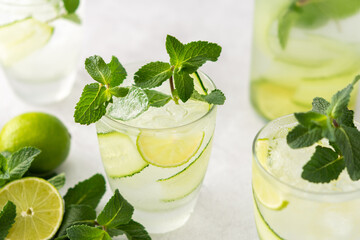 Cold refreshing drinks with lime and cucumber, summer iced beverage and fresh green mint, glass with lemon water close up
