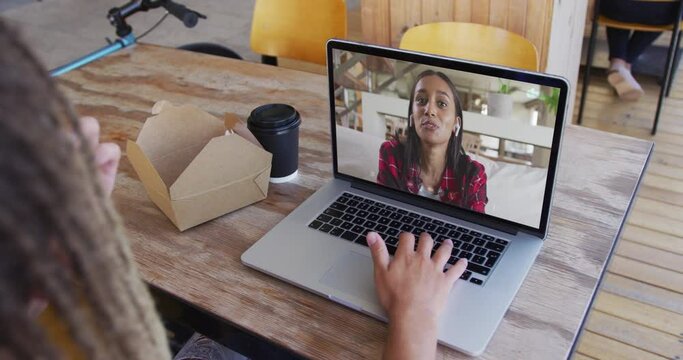 Woman having a snack while having a video call on laptop at a cafe