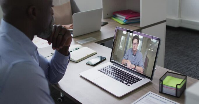 African american senior man having a video call with male colleague on laptop at office
