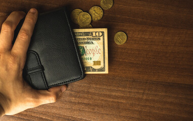 Man hold wallet with last savings money, ten dollar with cents in men's purse, wooden table background, top view photo with copy space