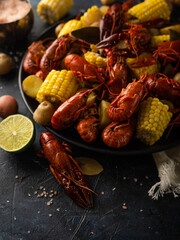 A hearty lunch - boiled crayfish, corn and lemon. Large black plate. Black dining table. Bright colors. Contrast. There are no people in the photo. Lots of bright colors.