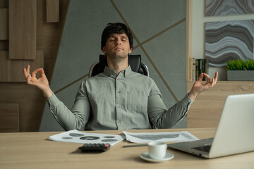 Man meditating in office coping with stress. Business executive doing yoga at desk in a modern...
