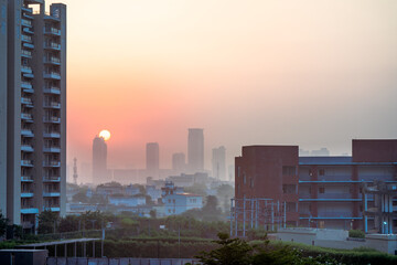 dawn shot of skyscraper and small houses in the background with tall buildings with homes offices hidden by fog in the background with the sun rising behind them