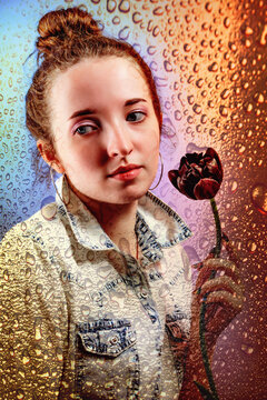 Abstract portrait of pensive girl with black tulip behind window glass with drops of rain and colorful reflection from rainbow or sunrise or sundown