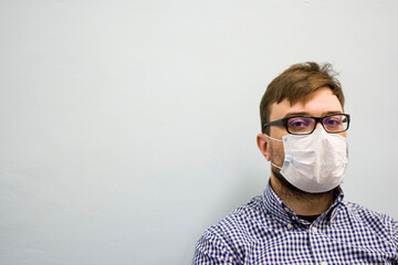 Portrait of a young man in glasses in a medical protective mask for a face on a light background and looking at the camera
