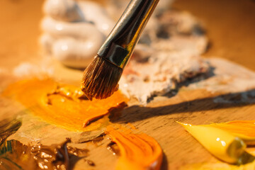 Artist work. Painting art. Professional craft. Paintbrush mixing orange white oil or acrylic paint colors on old stained wooden palette.