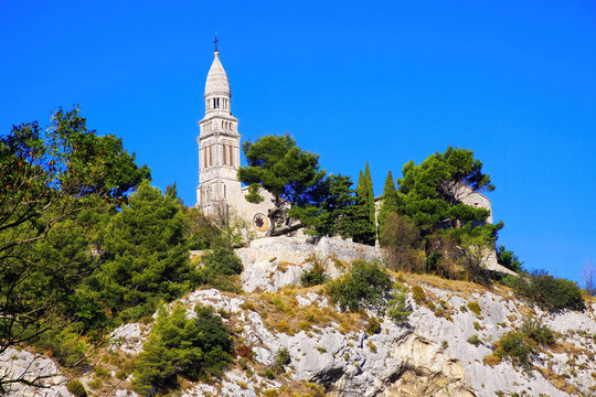 Low angle view on isolated roman catholic church on mountain peak with pine and cypress trees against blue sky - Plan d&acute;Orgon, Bouche du Rh&ocirc;ne, Provence, France
