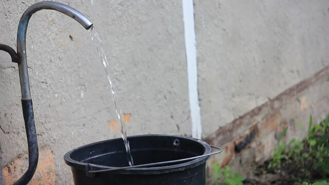 Collecting water from artesian spring with 20 litre plastic bucket using a pump from underground well