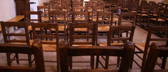 Fototapeta na wymiar View on isolated old brown wood chairs with backrest in a row inside catholic empty church illuminated by natural sun light (focus on backrest of chair in center))