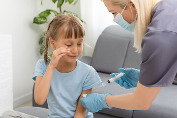 A little girl with tears in her eyes is very afraid of vaccination. The baby cries closing his eyes in pain. Portrait of a sobbing child who is injected in the shoulder. Children's medical concept,