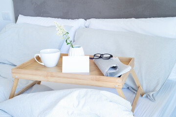 Breakfast in bed stationery mockup scene. Blank greeting card mockup, cup of coffee, newspaper and glasses on tray. White vase with small flowers. Valentine's day breakfast, lifestyle concept.