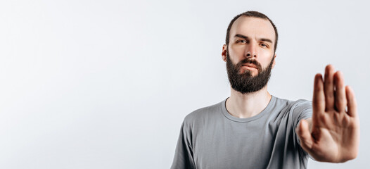 Fototapeta premium Portrait of handsome young man frowning while looking at camera holding hand opposite and saying stop gesture on white background with space for advertisement mock up