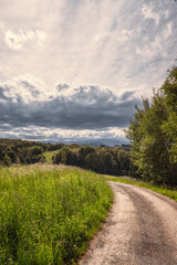 Inviting rural road, summer landscape with cloudy sky - 435696999