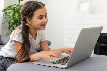 Distance learning. Cheerful little girl girl in headphones using laptop studying through online...