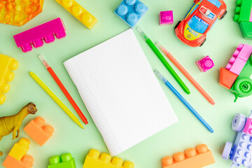 Back to school concept with exercise book, colorful pens, kid toys over mint green background.
