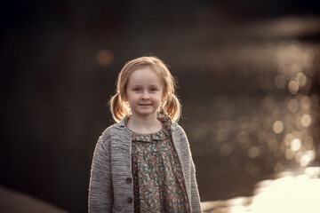 Portrait of a cute little girl with two ponytails during the sunset. Image with selective focus and toning