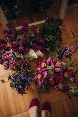 bright fresh beautiful bouquets on the parquet floor top view. female feet and flowers. bouquet of lilac and tree peonies top view.