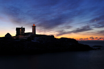 Moonset and the beginning of a winter sunrise over the Nubble Lighthouse on the coast of Maine