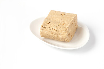 Sesame-peanut halva lies on a white plate on a white background. Traditional national dessert. Oriental, Turkish and Arabic cuisine.