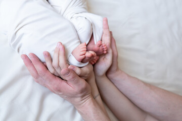 Fototapeta premium Mom and dad hands hold small legs of their two newborn twin babies