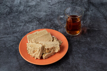 Peanut halva is on an orange plate, and there is a glass of armudu with tea next to it. Dark gray background. Traditional dessert. Oriental, Turkish cuisine.