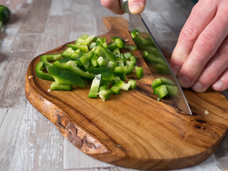 Cutting green pepper with a knife on a wooden board in the kitchen, close-up photo, warm color of the photo