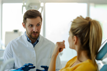 Handsome man dentist talking with his pretty patient.