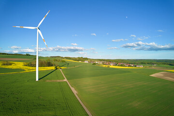 1 wind turbine on green farmland. Small village in the background. Blue sky with small moon. Aerial...